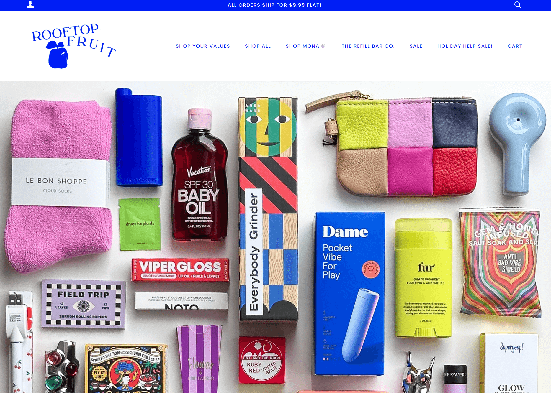 shopify general store: A colorful assortment of beauty, wellness, and lifestyle products arranged on a light surface, including socks, lip gloss, sunscreen, grinder, coin purse, vibrators, fur oil, playing cards, and soap. Rooftop Fruit logo at the top.