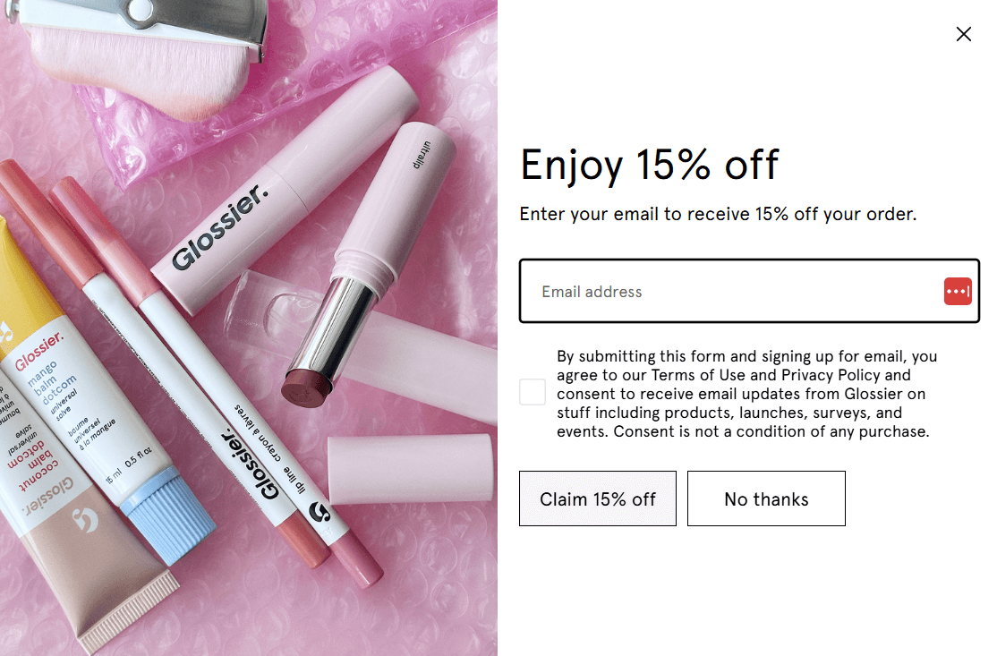 Marketing campaigns: A Glossier promo offering 15% off your first order with email sign-up appears beside pink Glossier makeup products, including a lipstick, brow pencil, and serum, all displayed on pink bubble wrap.