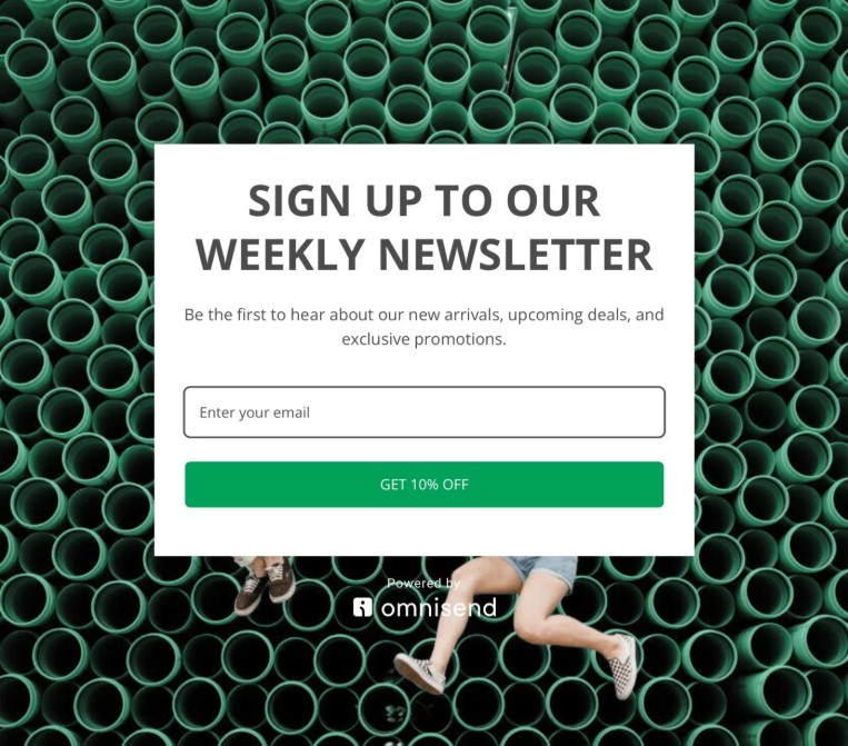 Email marketing for coaches: A newsletter sign-up form offers 10% off for entering an email, over a background of green pipes. Two people with bare legs and sneakers are partially visible at the bottom.