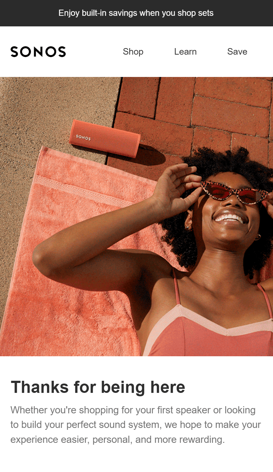 Welcome email template: A woman in a coral dress lies on a pink towel, smiling and adjusting her sunglasses. A portable Sonos speaker sits nearby on the ground. The scene appears sunny and relaxed.