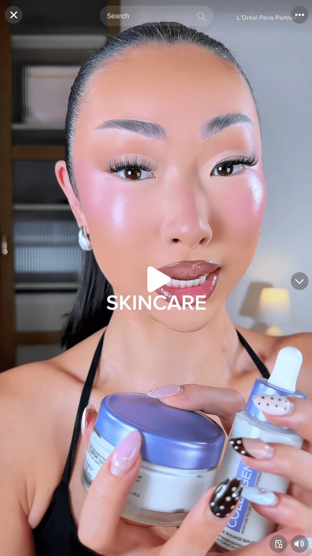 Testimonial advertising: A woman with glowing makeup holds a skincare jar and serum bottle, showing her glossy lips and manicured nails.