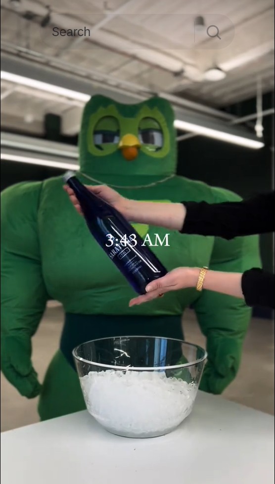 Guerilla marketing: A person pours liquid from a blue bottle into a clear bowl of ice, while someone in a Duolingo costume stands behind. The time 3:43 AM is overlaid on the image.