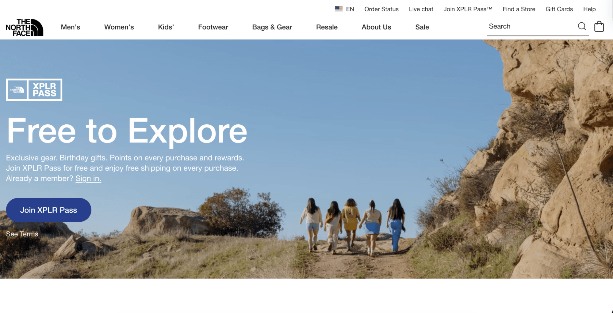 Loyalty programs: Five people walk up a dirt trail between rocky hills under a blue sky, featured on The North Face website promoting the XPLR Pass loyalty program with a Free to Explore headline and call-to-action buttons.