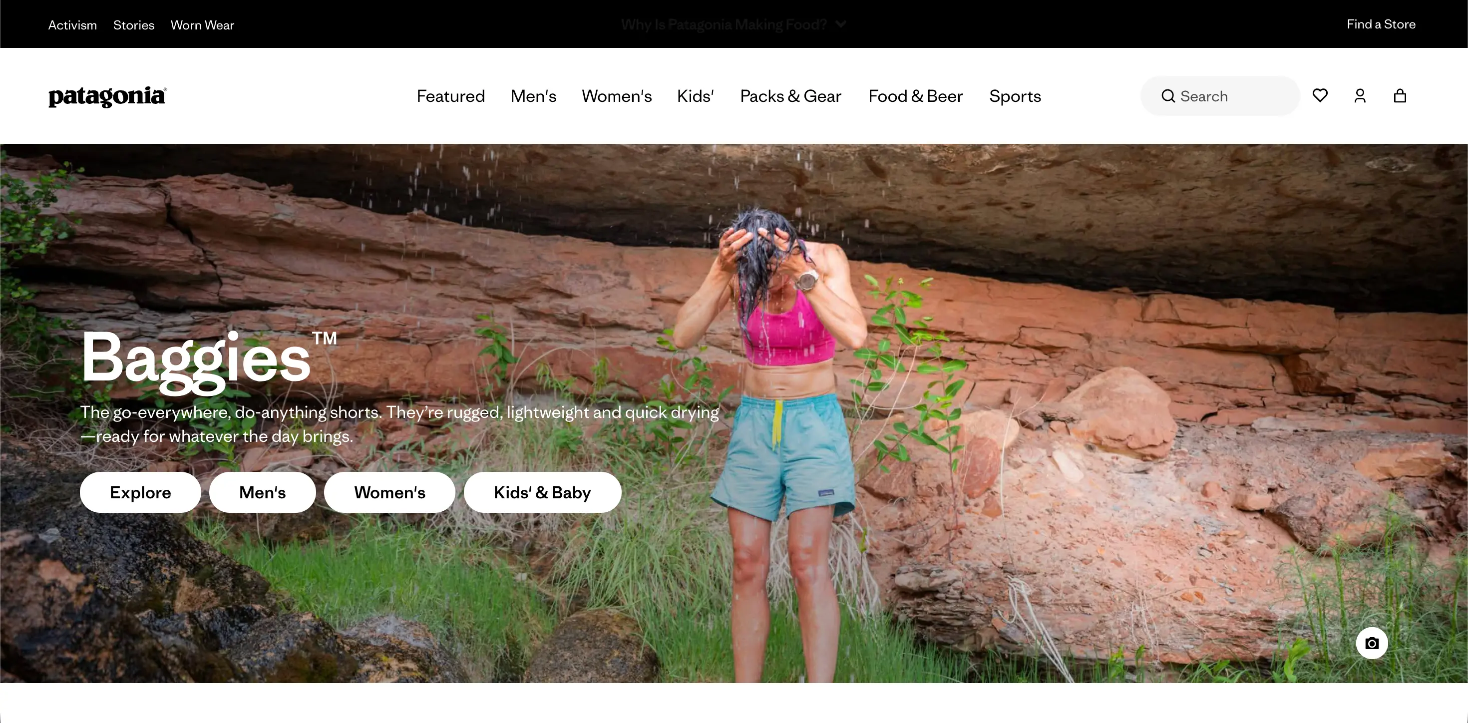 Person in pink top and blue shorts rinses head under water, standing outdoors near rocks and grass.