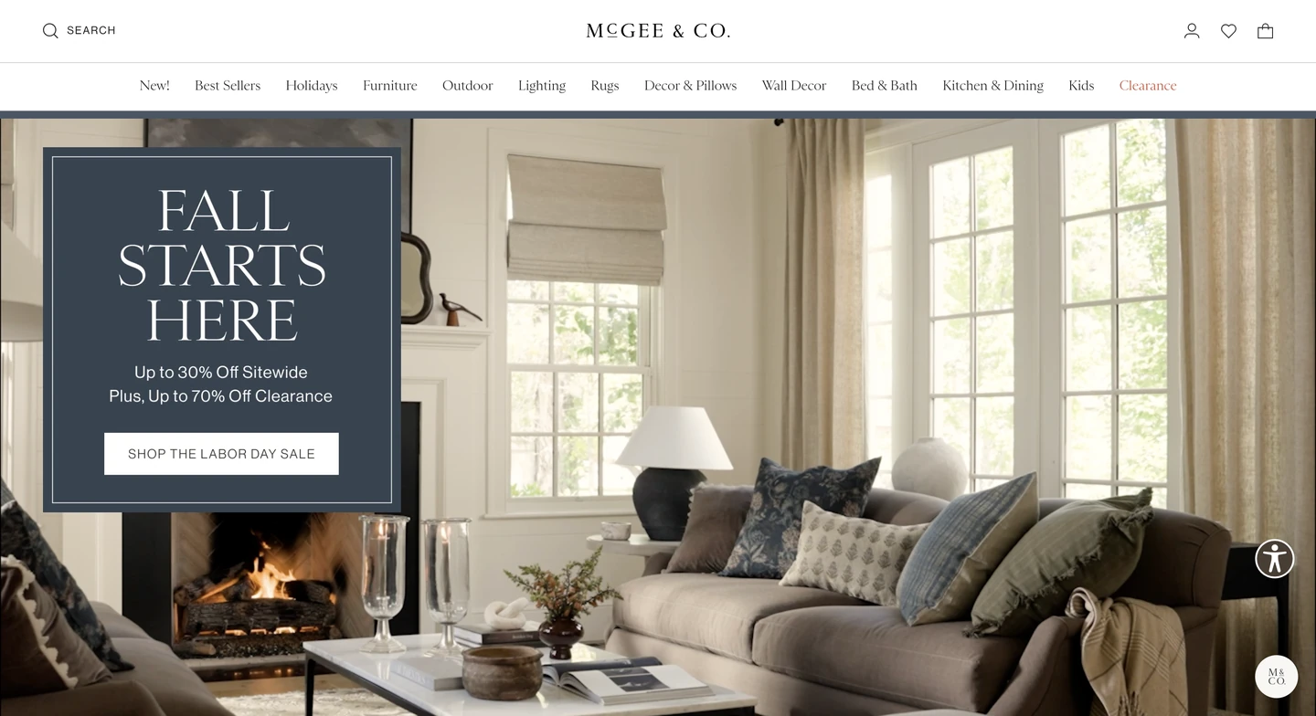 Living room with neutral decor, large windows, a lit fireplace, and a sale promotion sign on the left.