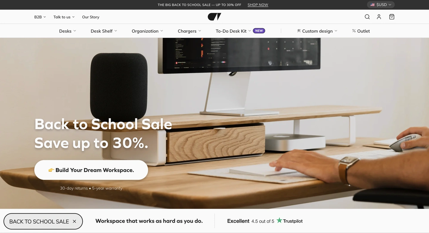 A person uses a mouse at a wooden desk with a monitor, speaker, keyboard, and drawer, promoting a back-to-school sale.