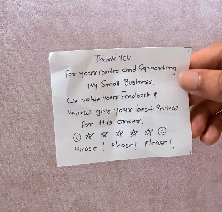 Hand holding a handwritten thank you note asking for a review and feedback for a small business order.