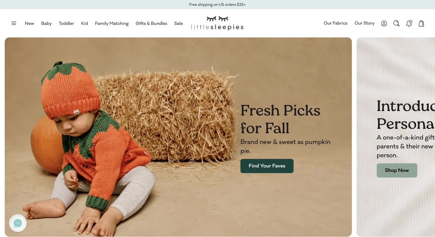 Baby in an orange pumpkin sweater sits on the floor next to a bale of hay, fall-themed background.