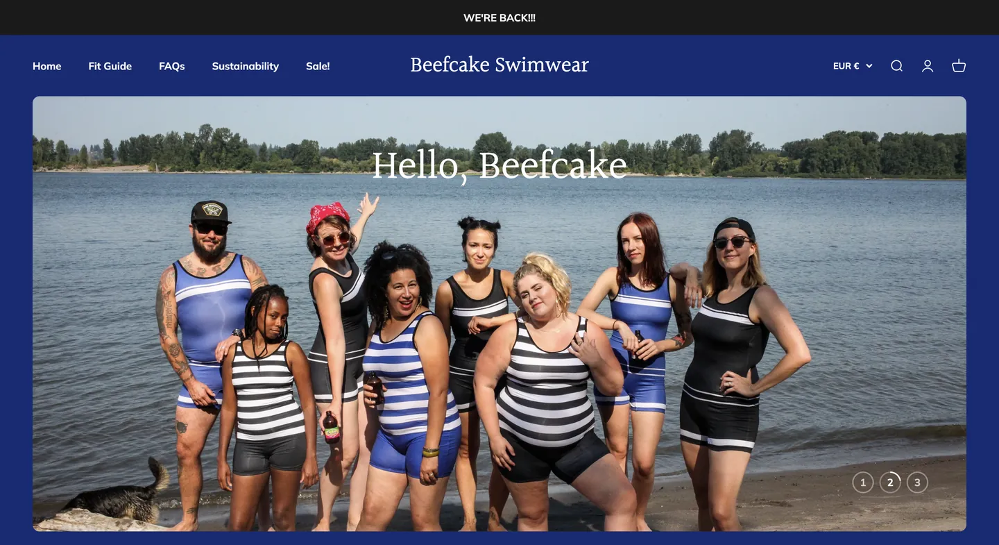 A group of people of various body types wear striped swimsuits while posing on a beach in front of a lake.