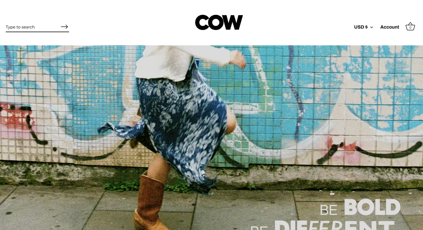 Person in a blue skirt and boots walks past a tiled wall with blue graffiti in an urban setting.